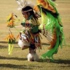 Native American figure in vibrant regalia dancing among flames