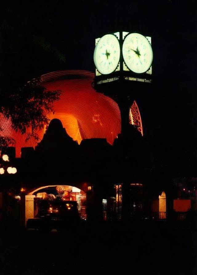 Night photo of building with red glow and green-lit clocks under dark sky