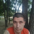 Contemplative man in red vest standing in forest with sunlight filtering through trees