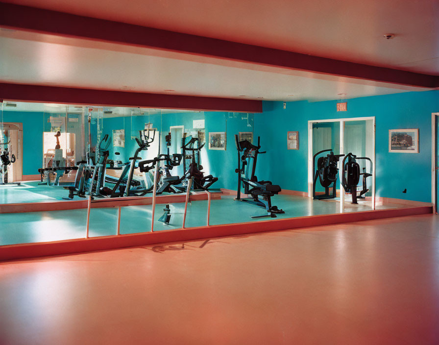 Brightly lit gym with turquoise walls, mirrors, exercise machines on red floor