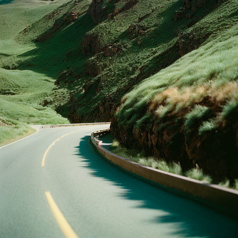 Scenic curvy road through lush green hills and sharp cliffs under a bright sky