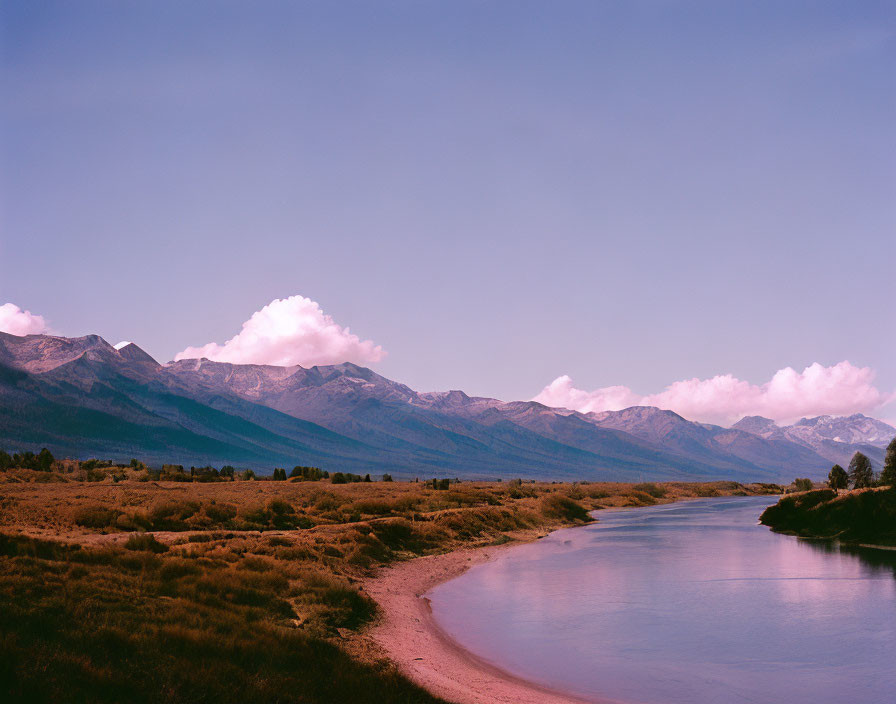 Tranquil river, grassy landscape, majestic mountains, pink-tinted sky