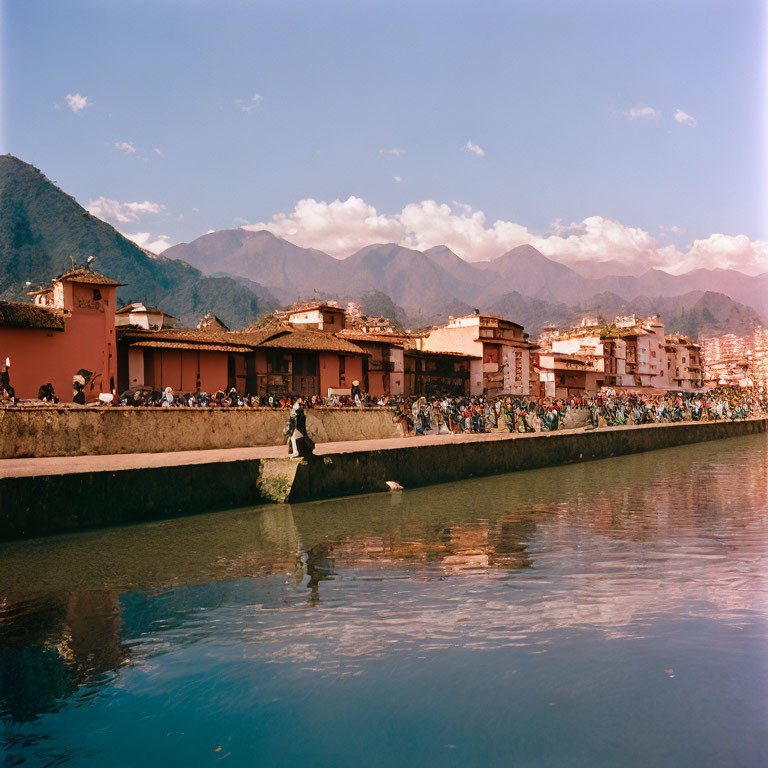 Riverfront with Terracotta-Roofed Buildings and Mountains in Background