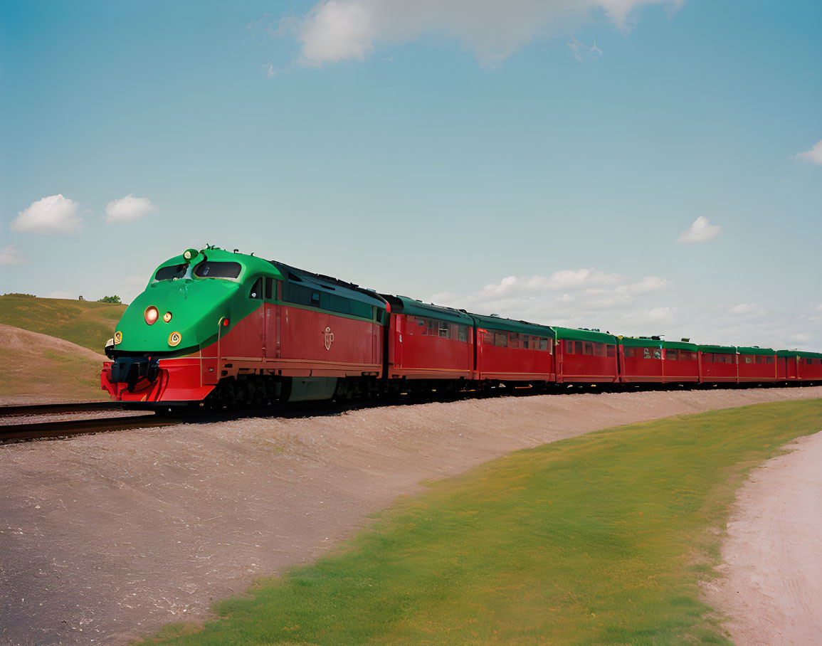 Vintage green and red locomotive pulling red carriages on railway under clear blue sky