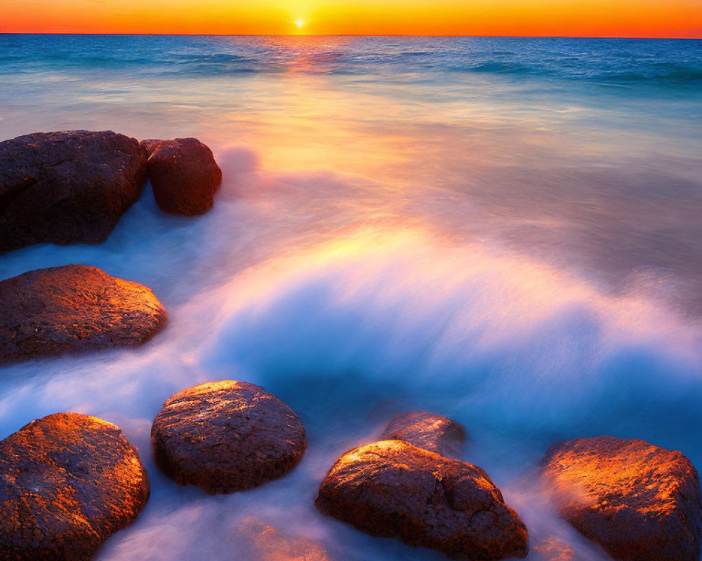 Tranquil sunset over sea with waves crashing on rocks under blue-orange sky