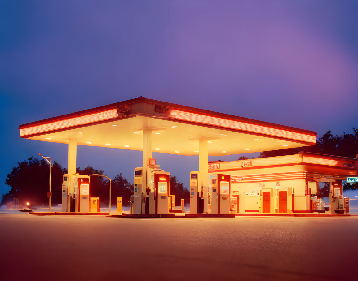 Gas station illuminated at twilight with clear skies, bright canopy lighting and fuel pumps