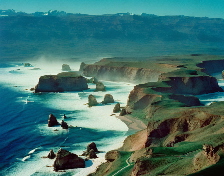 Coastal cliffs with arches and sea stacks under blue sky & crashing waves