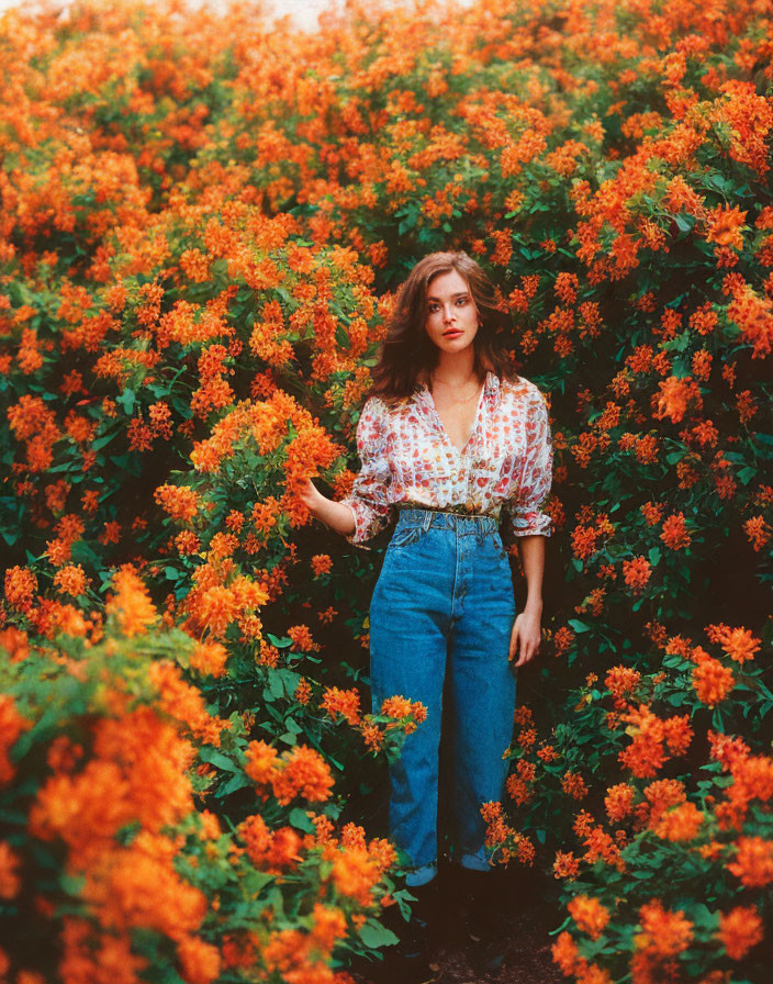 Woman in denim jeans surrounded by orange flowers and patterned blouse