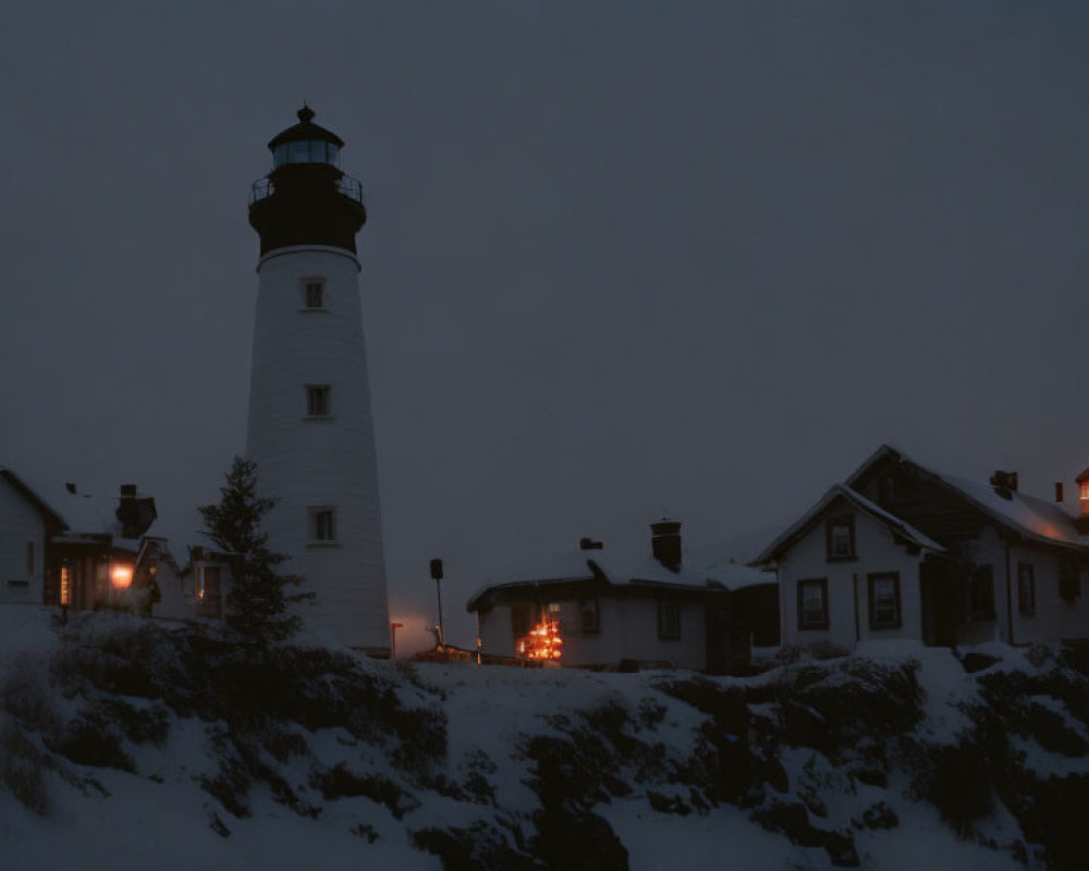 Lighthouse and buildings illuminated at twilight with snow-covered rocky terrain