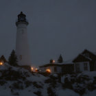 Lighthouse and buildings illuminated at twilight with snow-covered rocky terrain