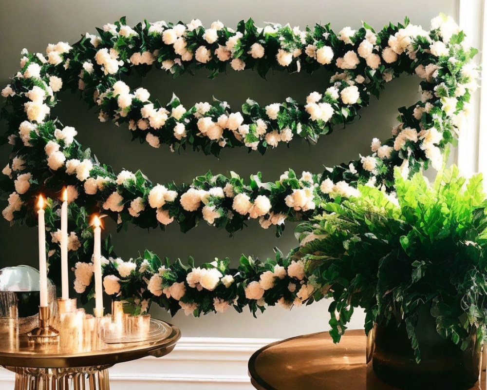 Floral wreath with white flowers and green leaves above table with candles and plants