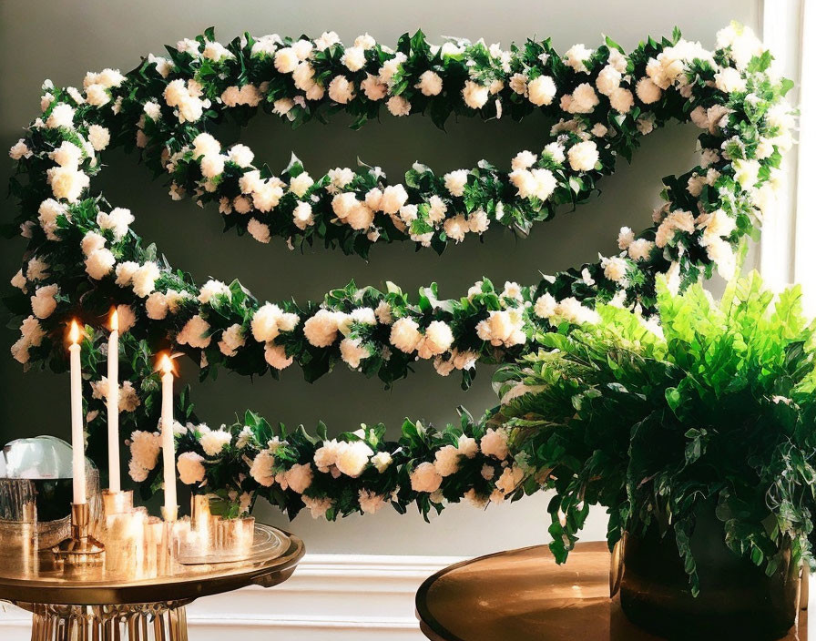 Floral wreath with white flowers and green leaves above table with candles and plants