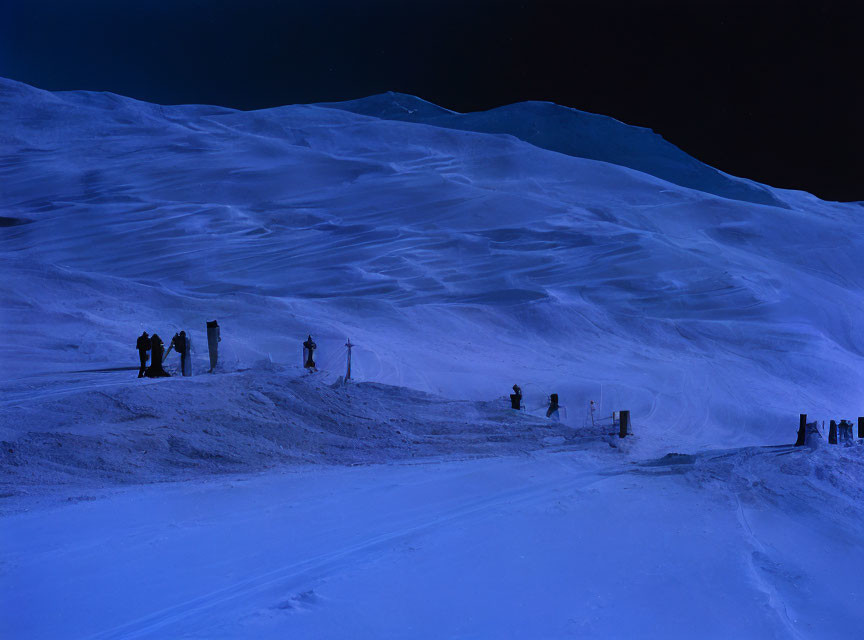 People standing on snowy mountain slope at twilight with blue-tinted snow and darkening sky