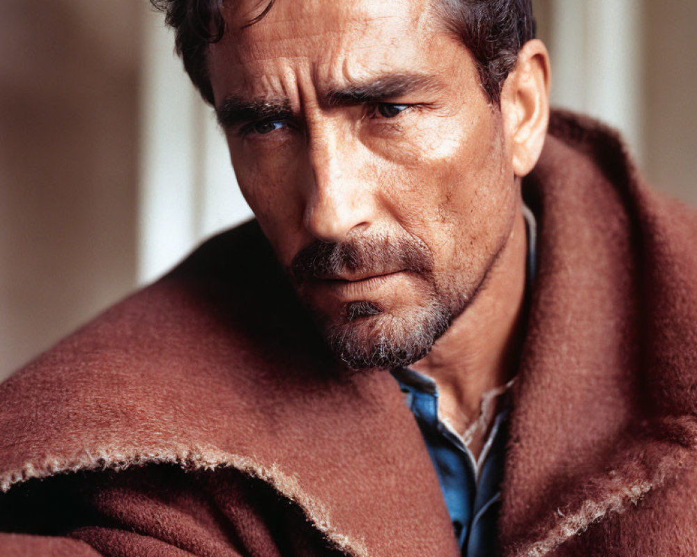 Intense man in poncho with stubble and furrowed brow