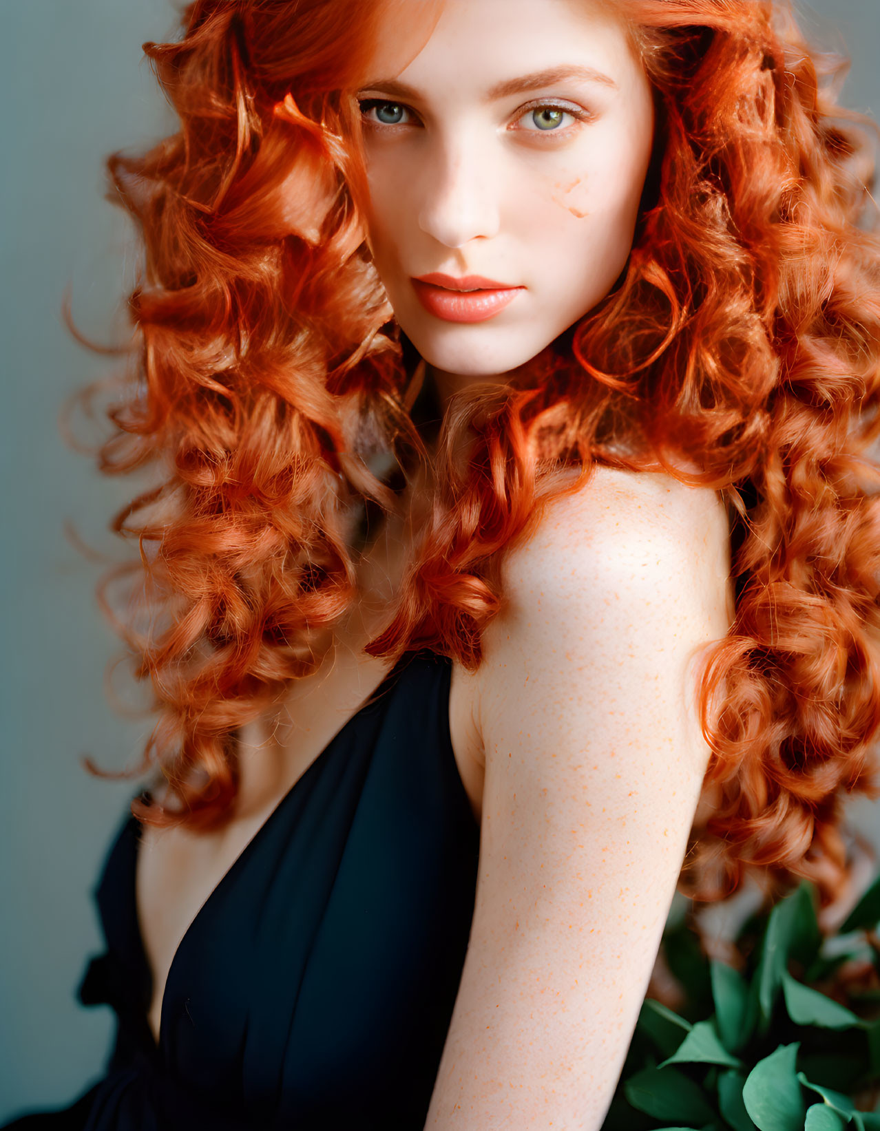 Red-haired woman in black outfit with freckles gazes over shoulder in nature setting