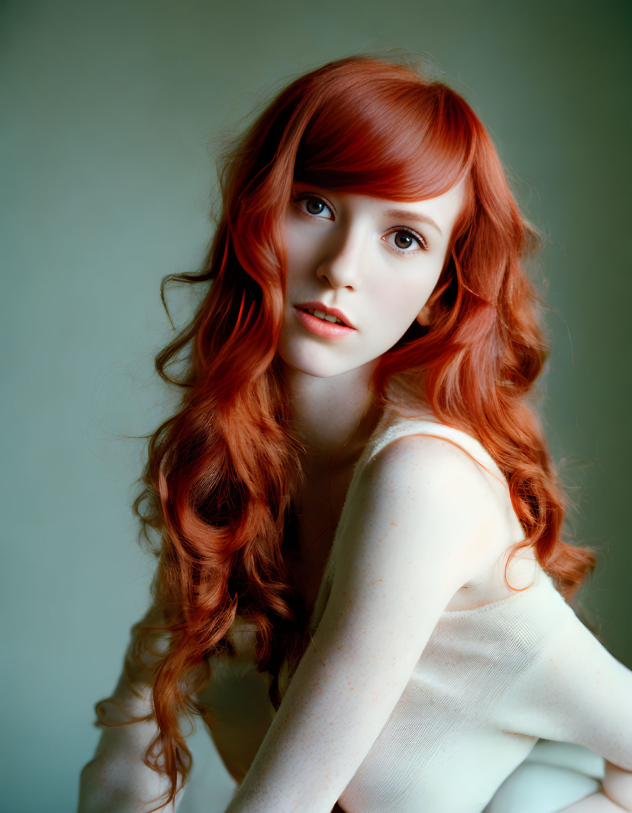 Red-haired woman in white top against green background poses with freckles.