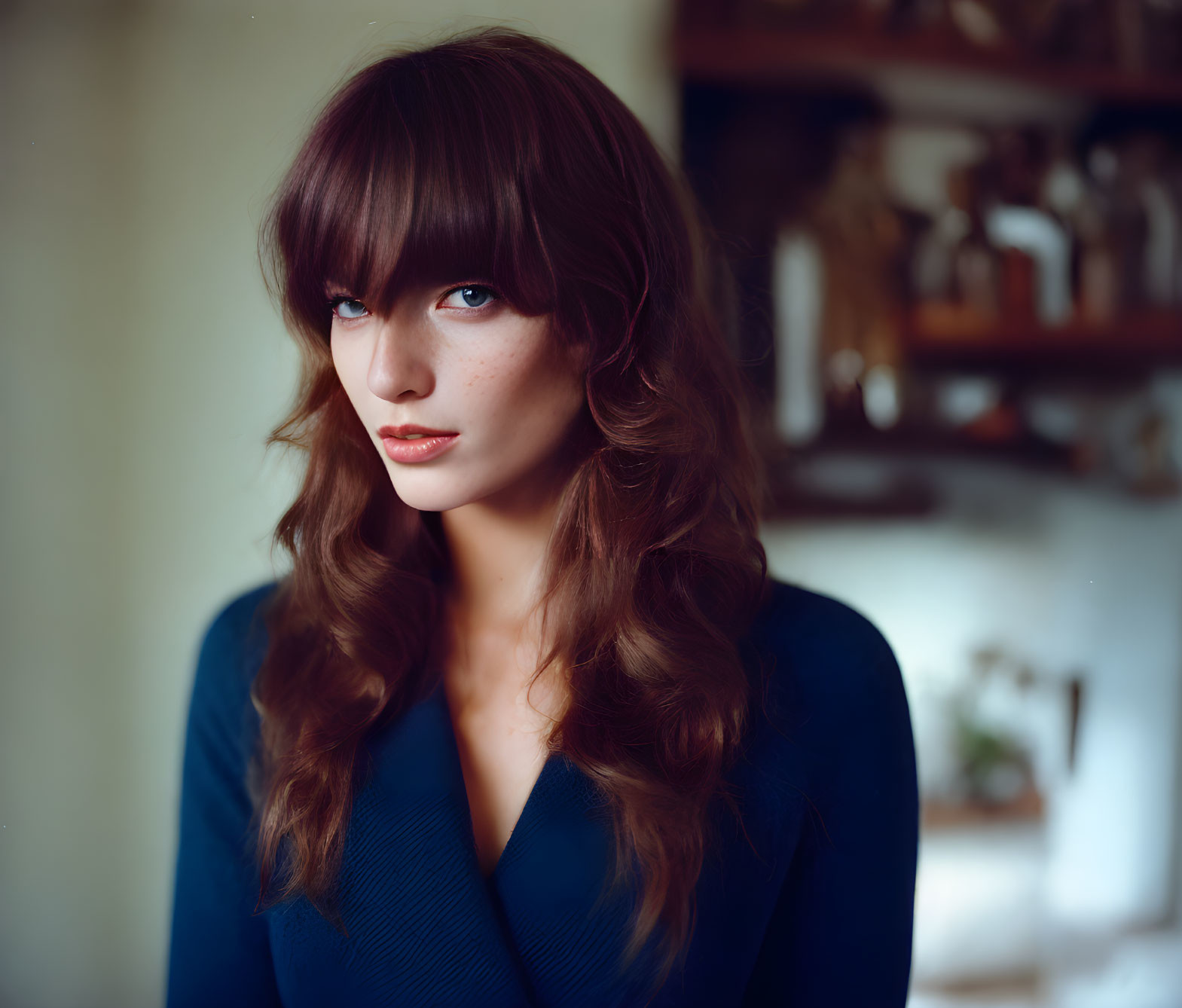 Brown-haired woman in blue top gazes softly at camera indoors