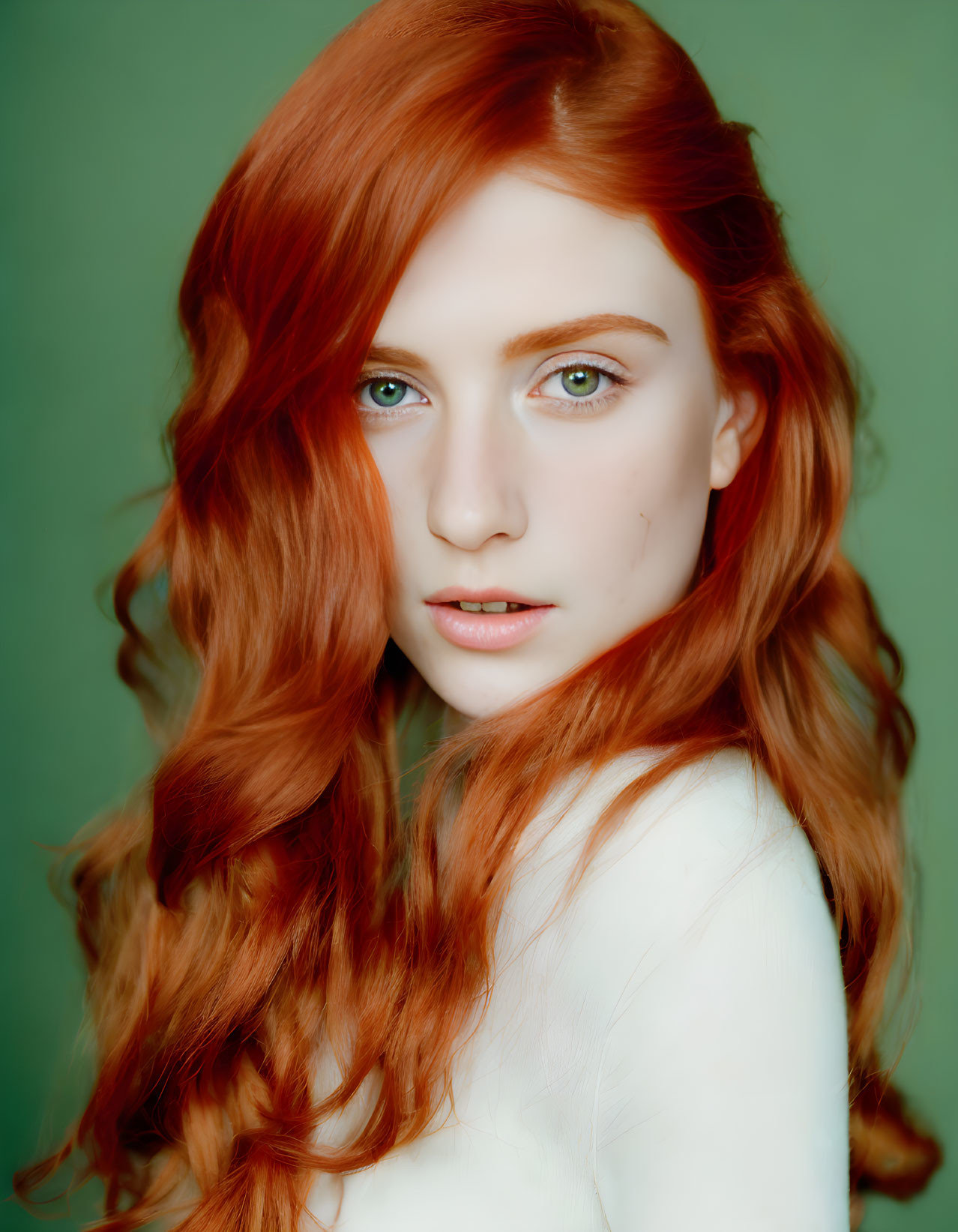 Portrait of woman with long red hair, fair skin, and blue eyes against green background