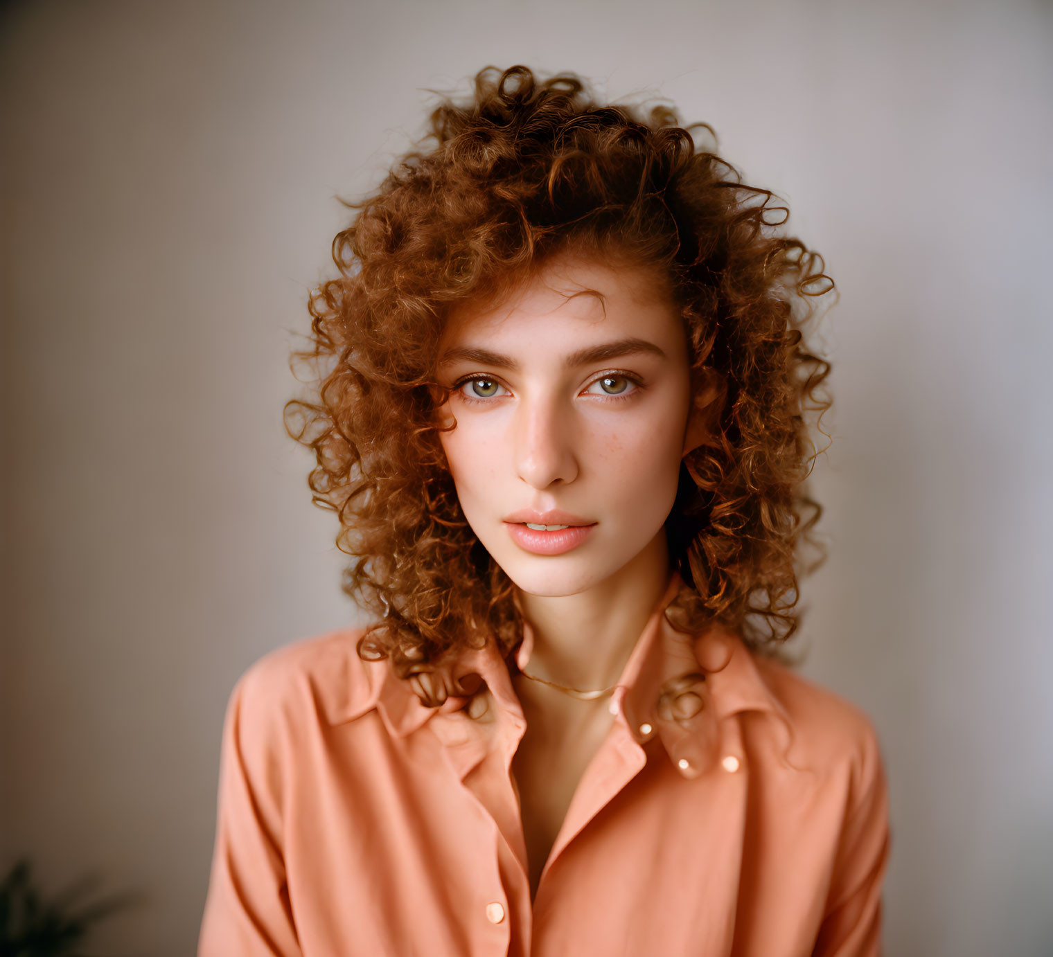 Curly-Haired Woman in Peach Shirt Gazes at Camera