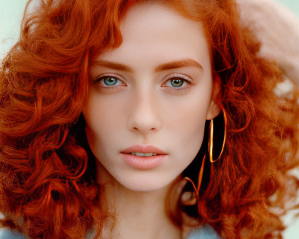 Vibrant red curly hair woman with blue eyes and gold earrings in turquoise coat