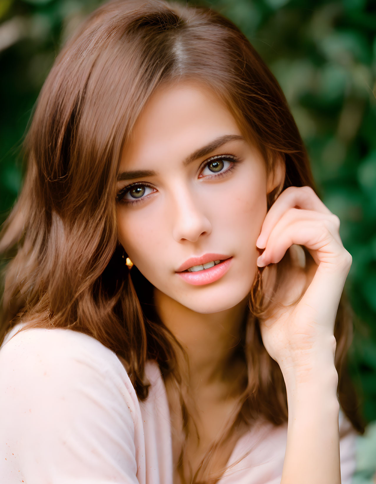 Brown-haired woman with hazel eyes and light makeup posing against green background