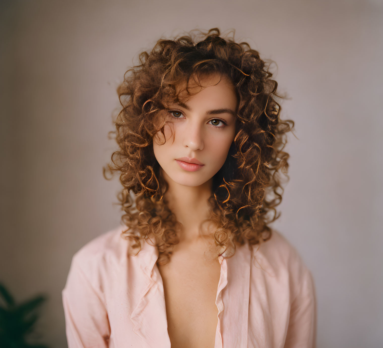 Portrait of young woman with curly hair and pink blouse in soft-focus setting