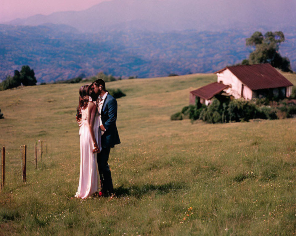 Embracing couple in green field with rolling hills and house under clear sky