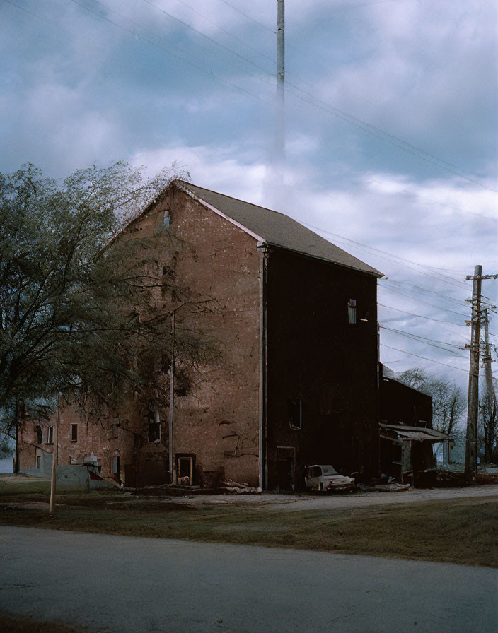 Brick building, cloudy sky, bare trees, utility pole, parked car