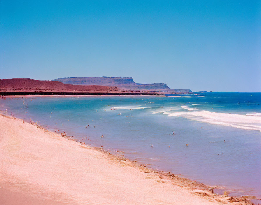 Scenic sandy beach with crystal blue waters and distant swimmers under clear sky