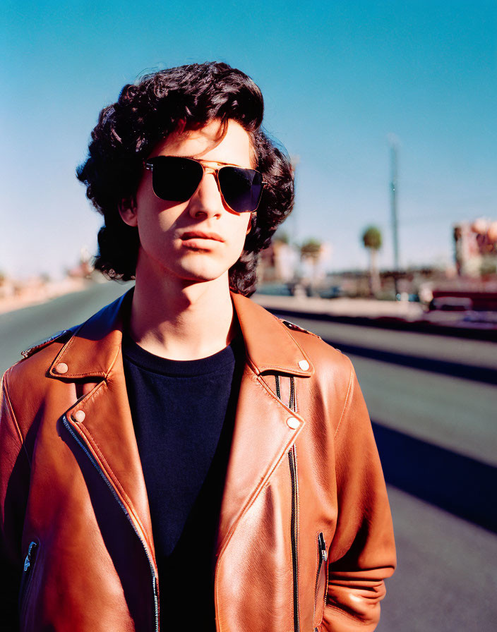 Curly-Haired Person in Sunglasses on Sunlit Road