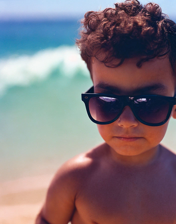 Child with Curly Hair Wearing Sunglasses at Beach