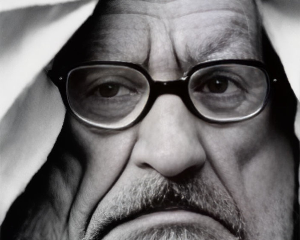 Elderly man with beard and glasses looking through torn paper