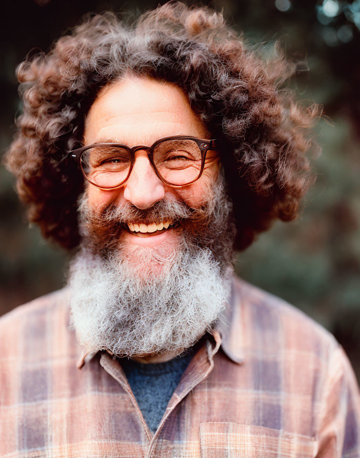 Cheerful man with curly hair and gray beard in plaid shirt and glasses smiling