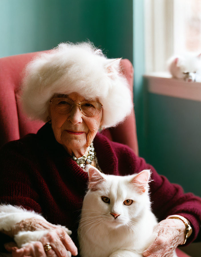 Elderly woman in red sweater holding white cat by window