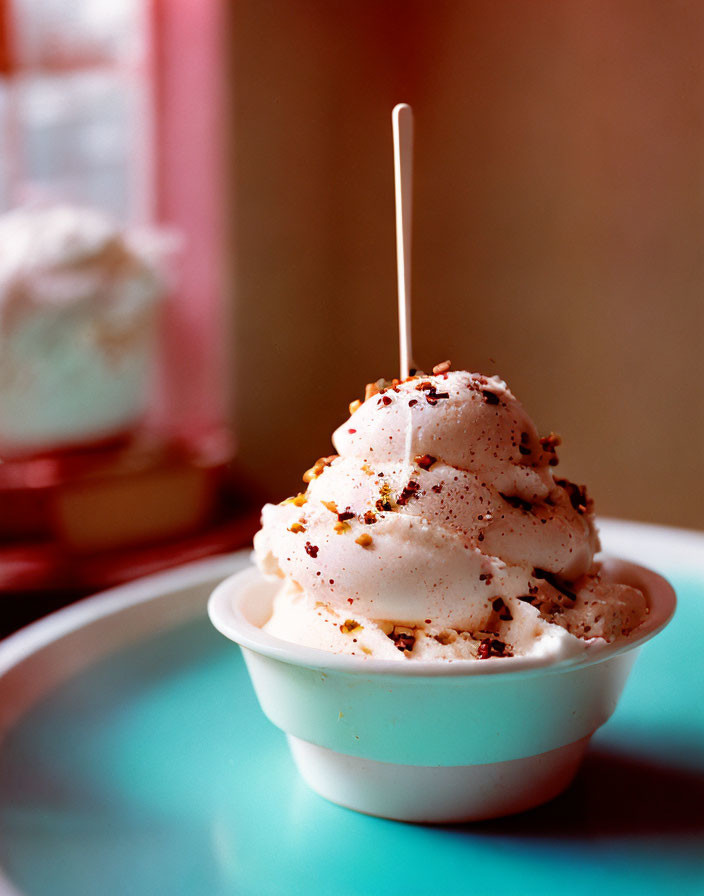 Swirled soft serve ice cream in white bowl with sprinkles and spoon on blurred background.