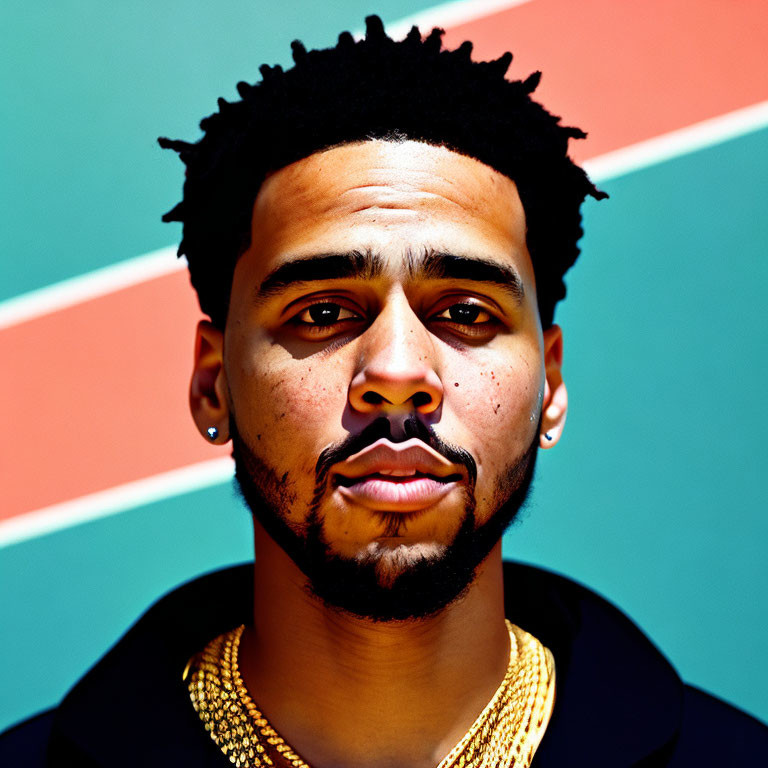 Young man with short dreadlocks and gold chain necklace against orange and teal background