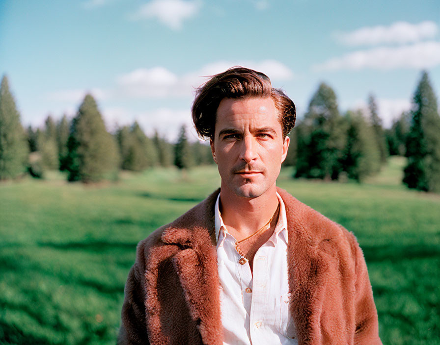 Man in Brown Fur Coat Standing in Field with Trees and Blue Sky