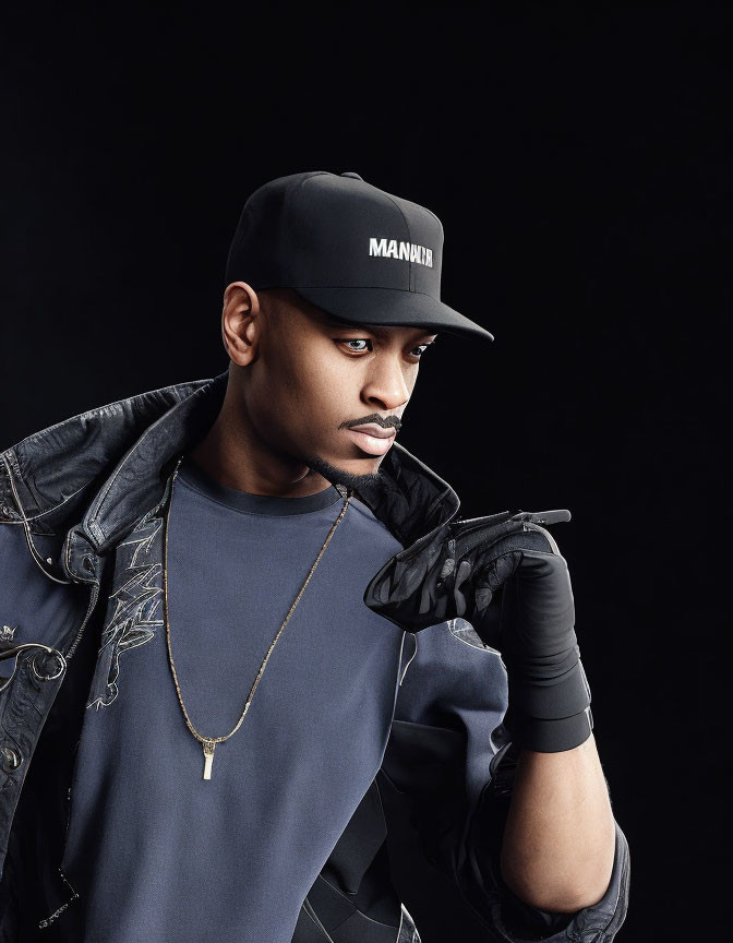 Fashionable Man in Black Outfit with Gold Chain Poses Against Dark Background