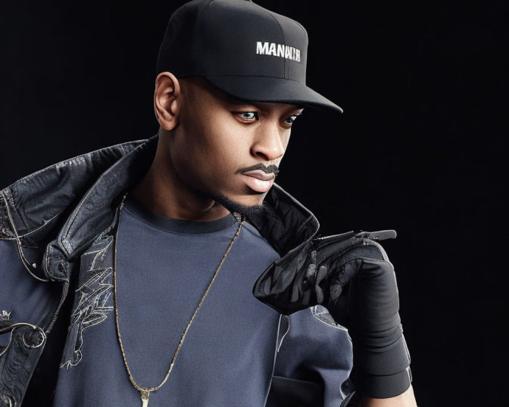 Fashionable Man in Black Outfit with Gold Chain Poses Against Dark Background