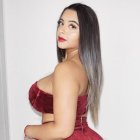 Woman with ombre hair in red outfit poses in modern room with shelves and safe