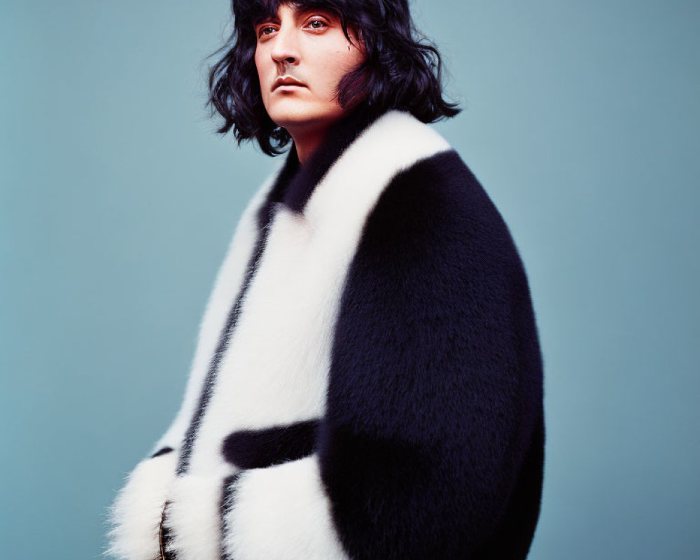 Serious person in black and white fur coat on teal background