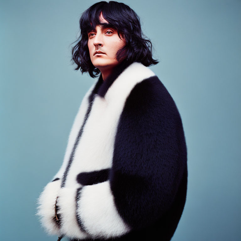 Serious person in black and white fur coat on teal background