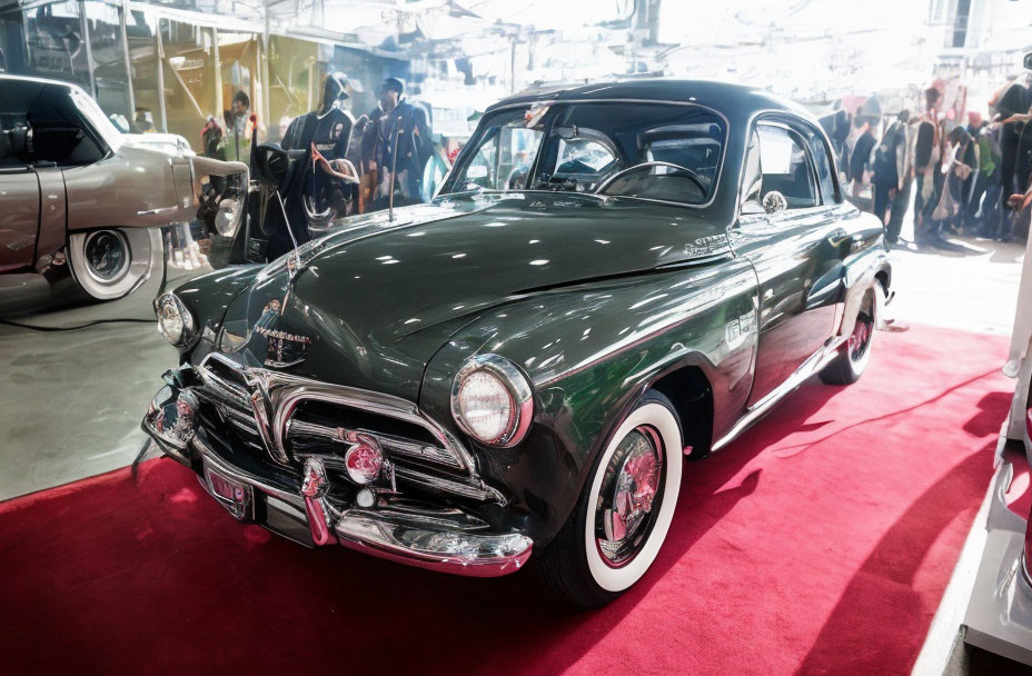 Classic Green Car Displayed at Indoor Car Show with Red Carpet and Classic Cars in Background