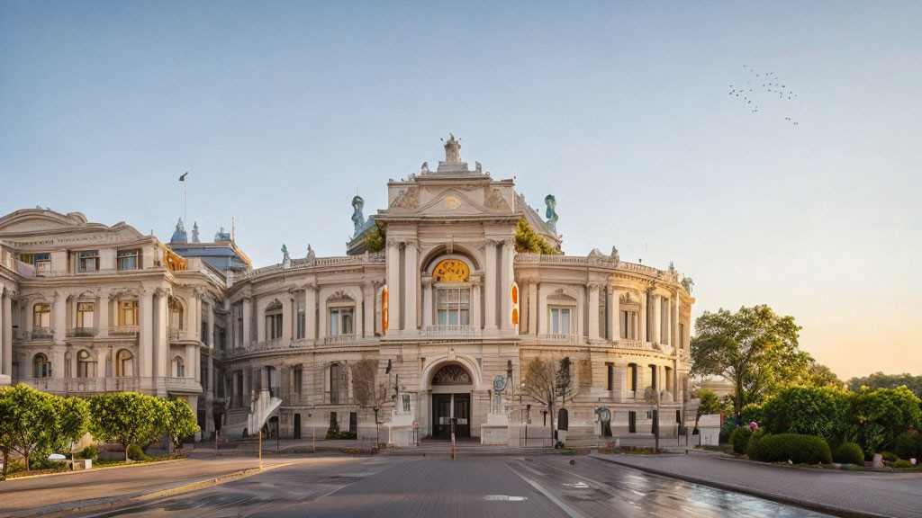 Neoclassical building with ornate facade and sculptures under clear sky at golden hour