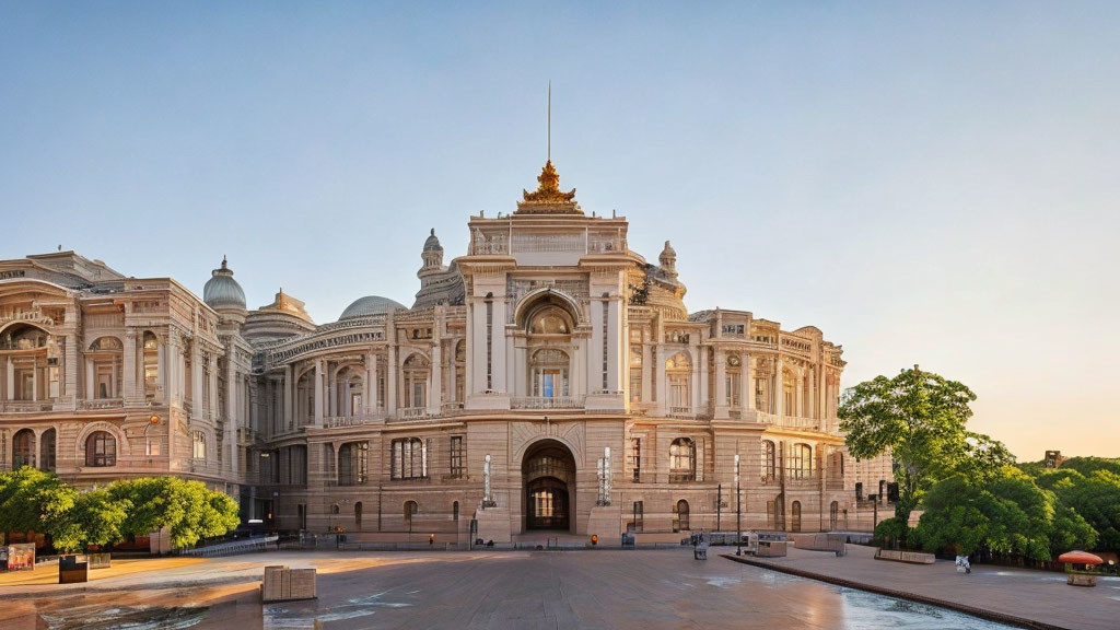 Neoclassical building with archway, sculptures, and gilded details at sunrise.