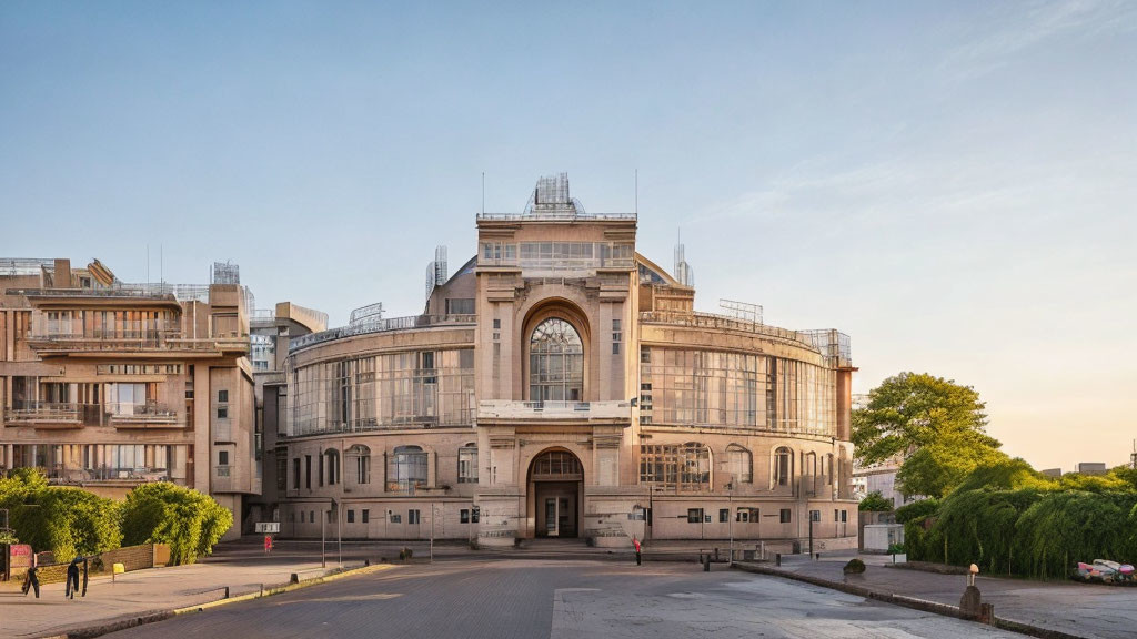 Grand arch entrance and symmetrical wings of historic building at dusk with people passing by