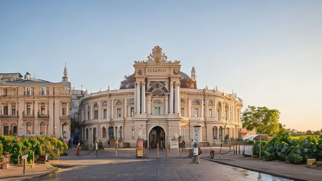 Historical building with arched entrance, statues, and greenery under clear sky at golden hour