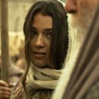 Young woman with long hair and headscarf in historical/fantasy setting with blurred figures