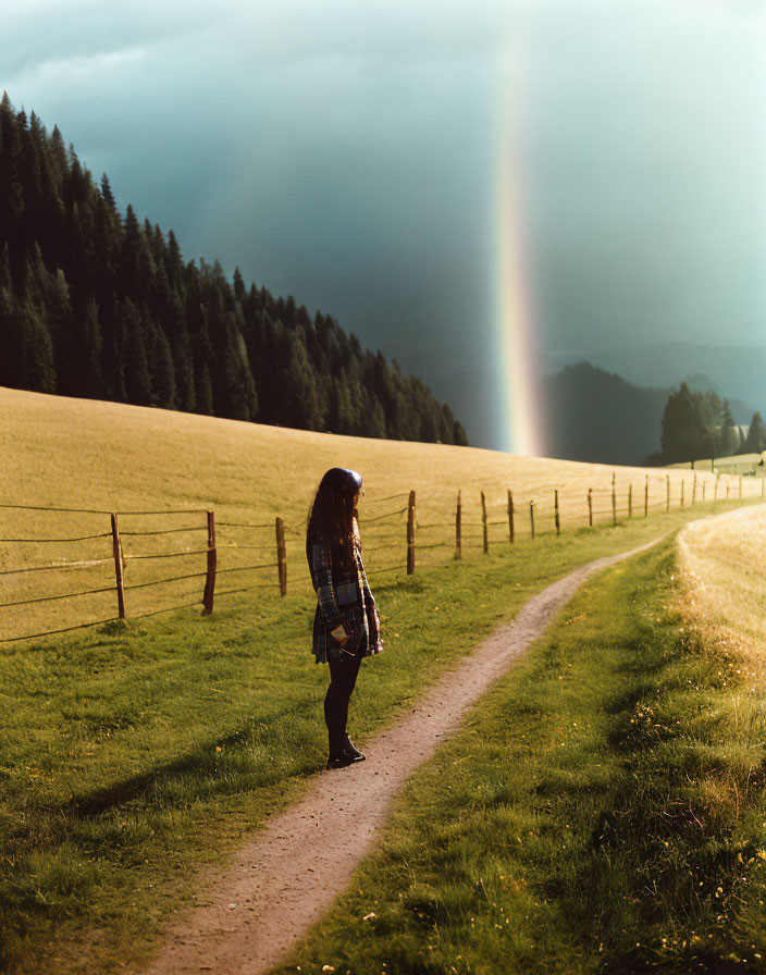 Person admiring rainbow over forest on cloudy day