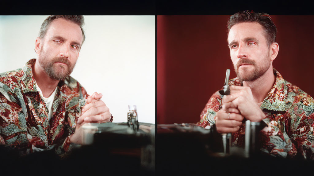 Bearded man in printed shirt holding pen, looking at miniature object